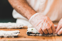 Close up of chef rolling sushi with sanitary gloves on