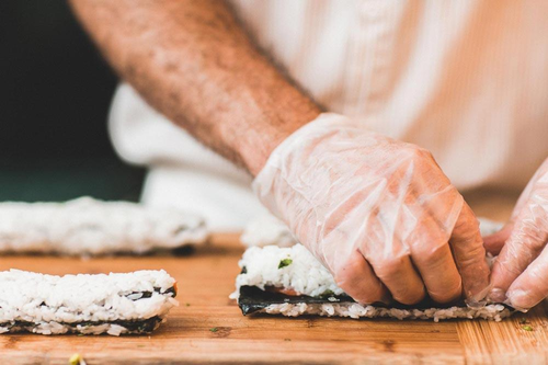 Close up of chef rolling sushi with sanitary gloves on