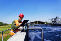 Man with hard hat and high vis vest surveying water at water treatment facility